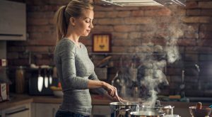 Vrouw kookt en er komt damp met kookgeurtjes uit de pannnen