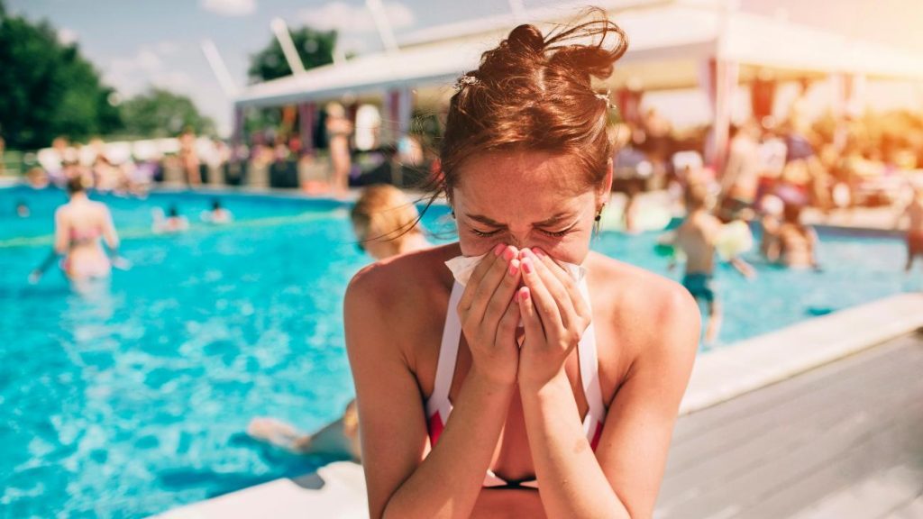 vrouw snotterend naast het zwembad, ziek op vakantie
