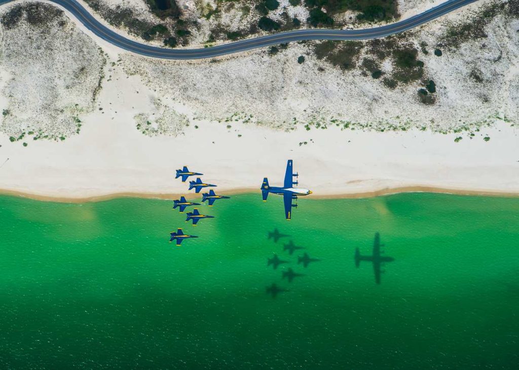 De Blue Angels maken samen met een C-130 een formatievlucht boven een kustlijn, geschoten door defensiefotograaf Cody Hendrix